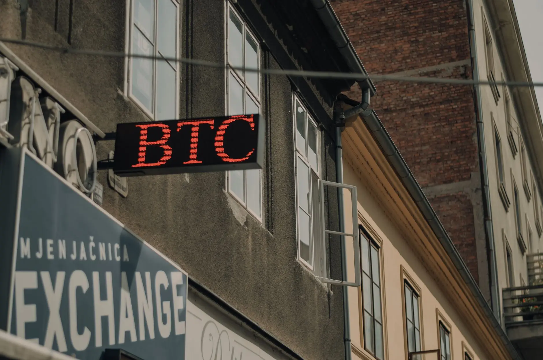 Sign displaying 'BTC' indicating a Bitcoin exchange in a city setting.