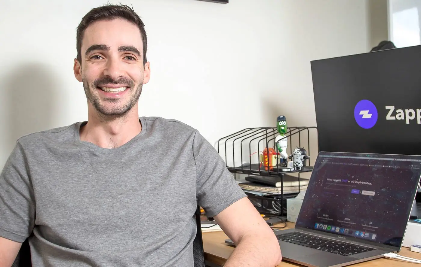 Man sitting at a desk smiling, with a Zapper logo in the background.