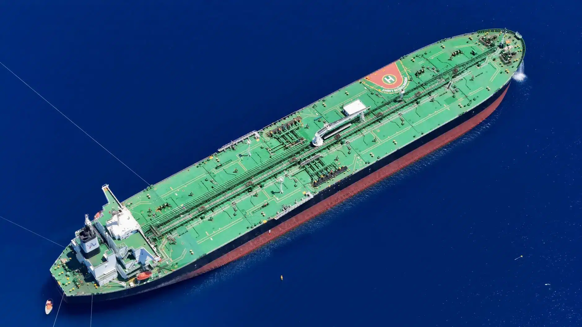High-angle aerial view of a large green and red oil tanker ship sailing through deep blue ocean water