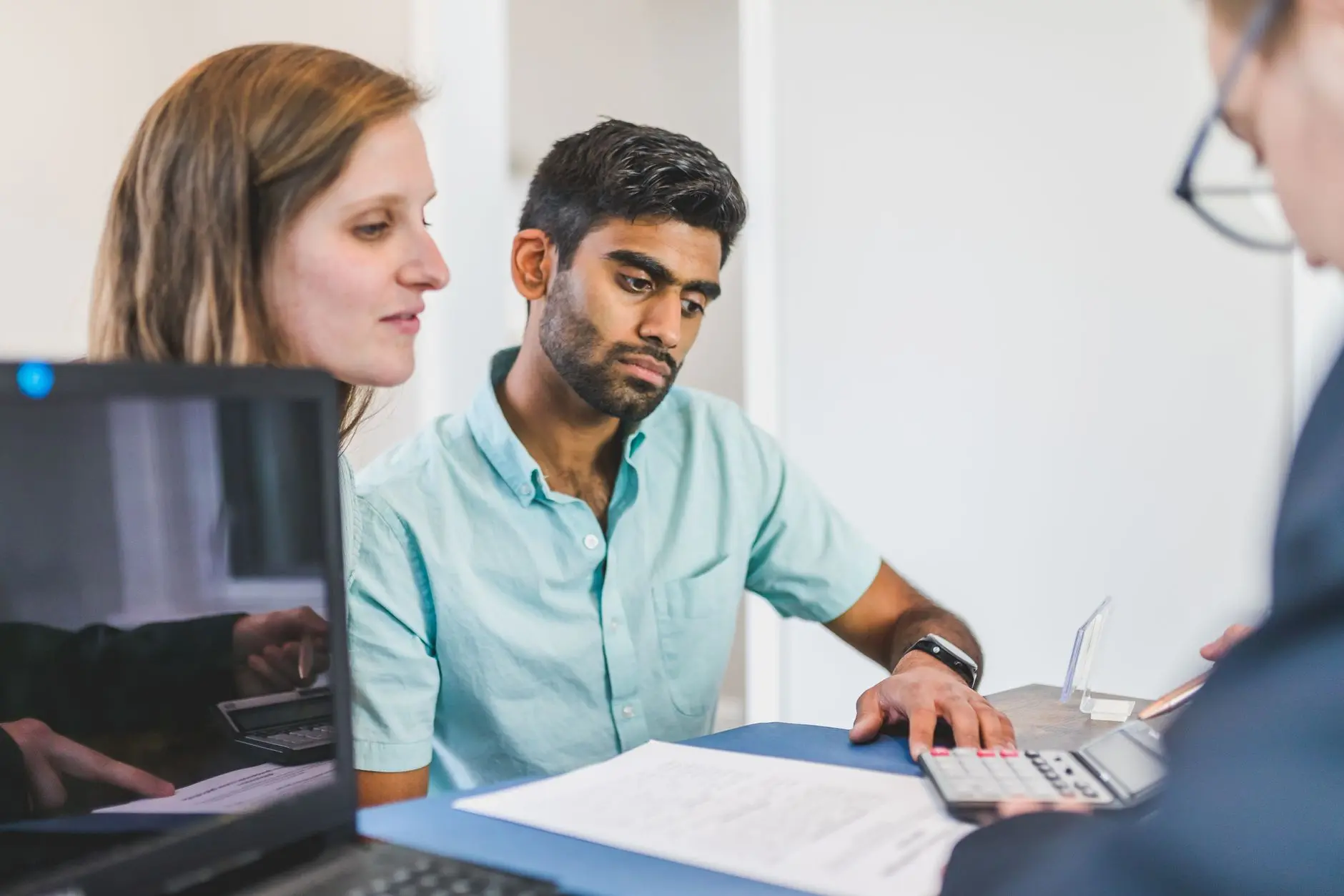 A financial advisor consulting with a client, reviewing documents and using a calculator.